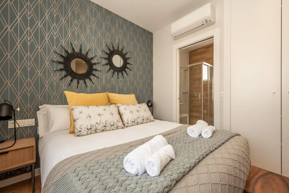 Chambre élégante avec lit double, coussins jaunes et salle de bain attenante, préparée pour accueillir les voyageurs.